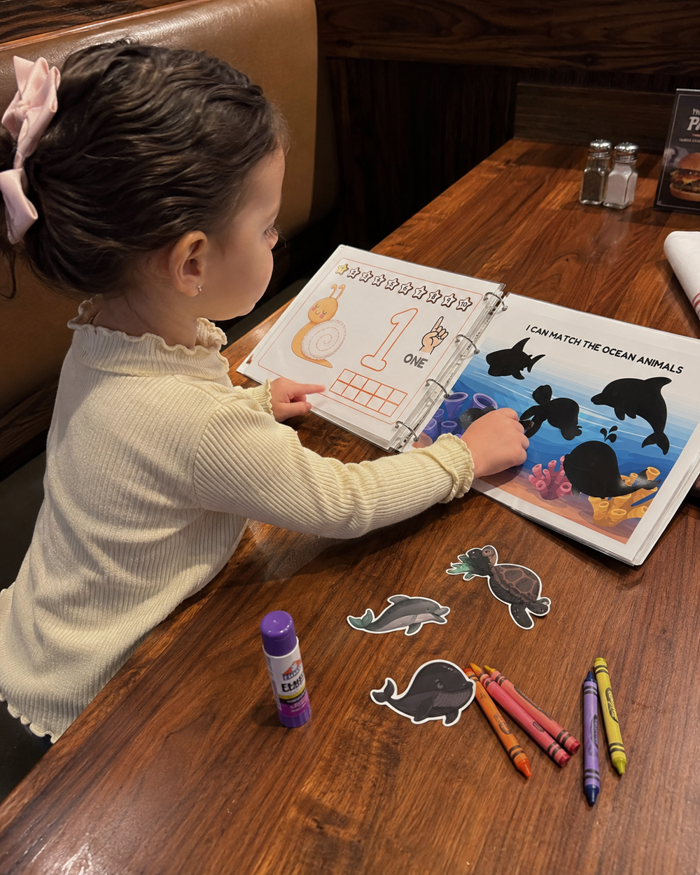 Girl matching ocean animal printables in an activity binder at a restaurant table